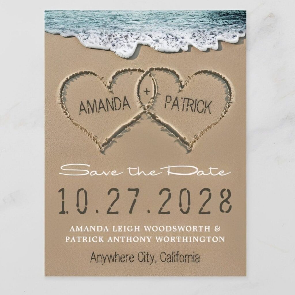 Beach destination save the date card featuring hearts drawn in the sand with ocean waves and a romantic coastal wedding theme.