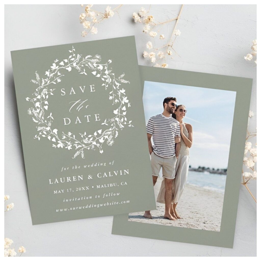 Sage Green Floral Wreath Save the Date Card featuring a delicate white botanical wreath on a sage green background with a personalized engagement photo on the back.